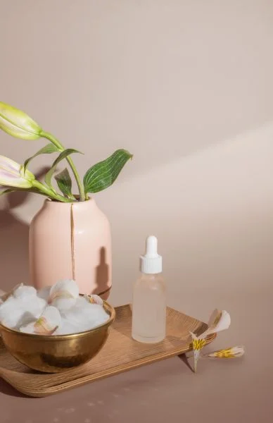 A minimalist skincare setup with a pink vase, plant, dropper bottle, and skincare spatula.